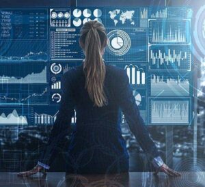 Image of woman looking at a large screen showing chart and graphs. A data lake is used with a data warehouse to support an organization's reporting requirements..