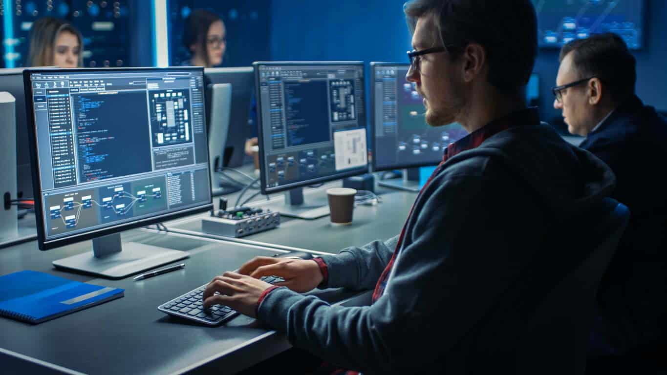 Smart Male It Programmer Working On Desktop Green Mock Up Screen Computer In Data Center System Control Room. Team von jungen Fachleuten Programmierung anspruchsvollen Code