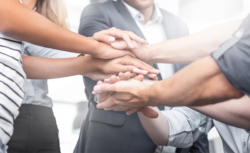 A Group of people gathered with their hands one on top of the other symbolizing the positive results in a team thanks to an emotionally intelligent leader.