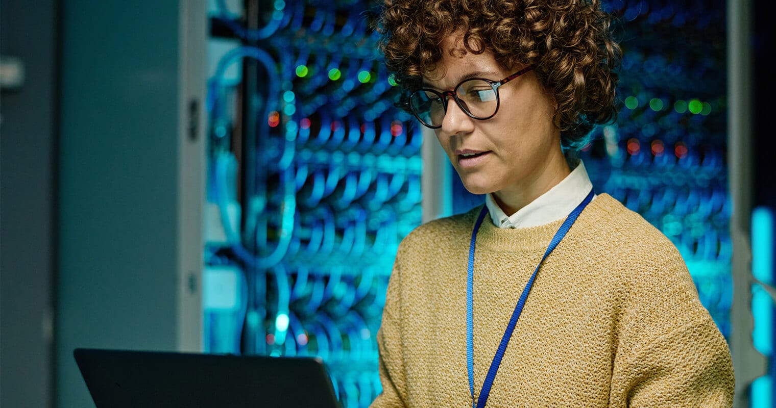 A tech professional woman analyzes cloud data innovation on a laptop in a server room