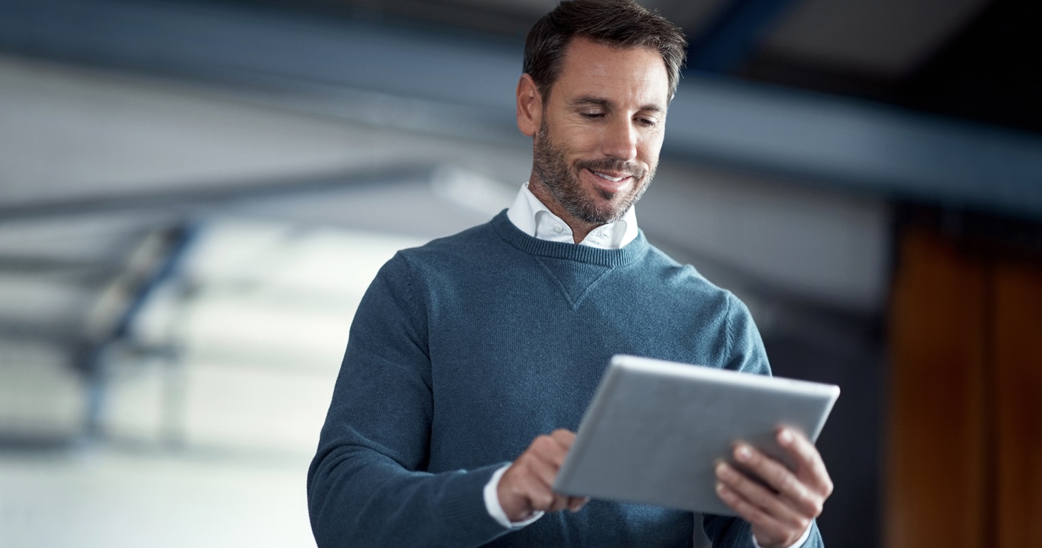 Man in sweater smiling at tablet, likely researching edge databases