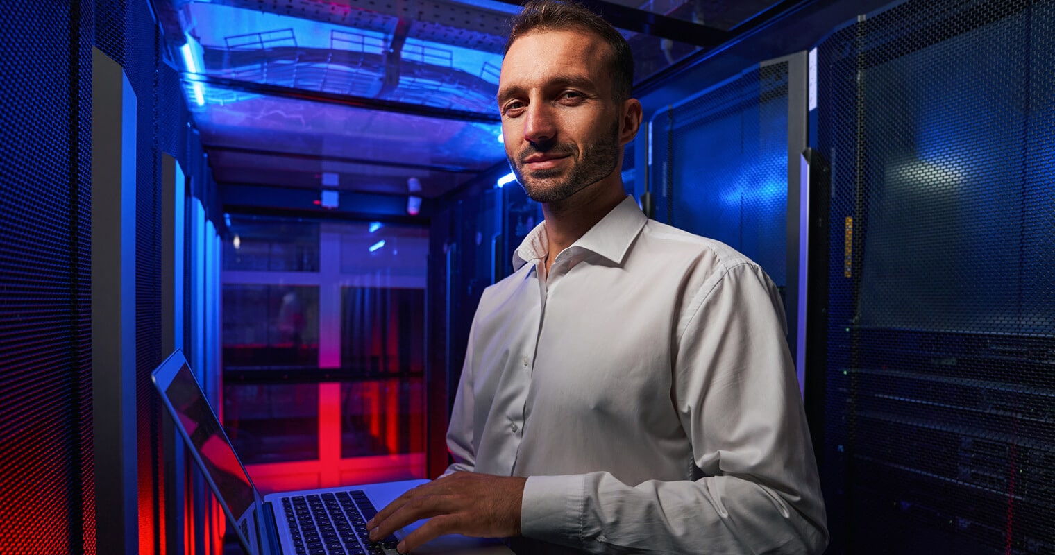 A man in a data center uses a laptop, managing systems for multi-cloud storage