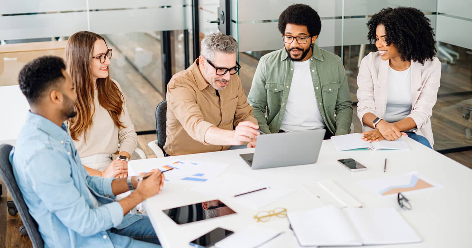 Ein Team arbeitet um einen Laptop herum und führt eine Diskussion. Die Szene spiegelt einen modernen Arbeitsbereich wider, der die Entwicklung ohne Code betont.