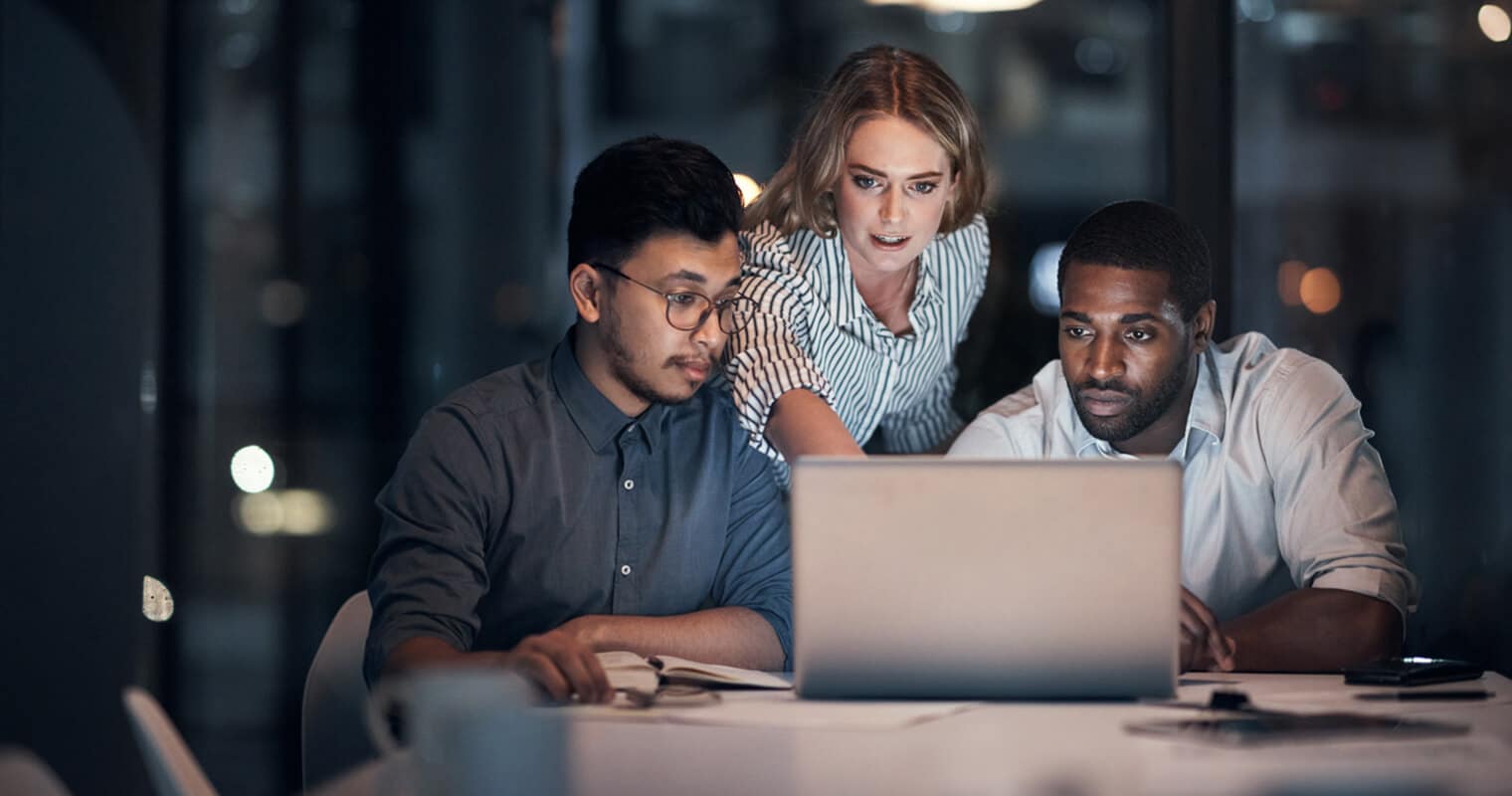 Trois professionnels collaborent tard dans la nuit autour d'un ordinateur portable, se concentrant sur la gestion des données par l'IA et analysant les stratégies pour une mise en œuvre efficace.